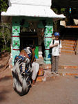 Maggie with a glass of tea outside a shrine.  (Maggie was here and Monica had started taking the photo when the worshipper suddenly appeared)
