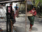 Ropemaking from coir - coconut fiber.  The hull is soaked and beaten.  The skin is pulled out of the smash, the fibers washed and fluffed.  The woman has a bundle of dried fibers which she feeds out to be twisted into a strand by the hand-operated machine